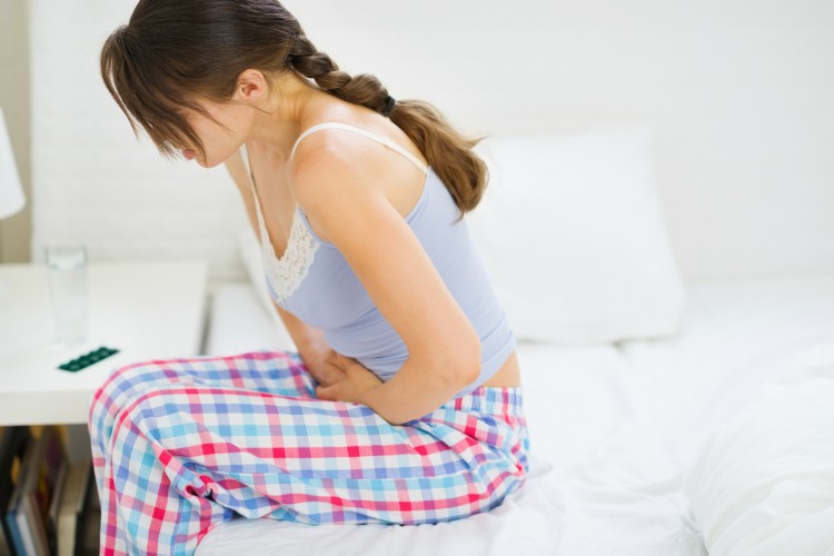 Image d'une fille sur un lit tenant l'estomac douloureuse